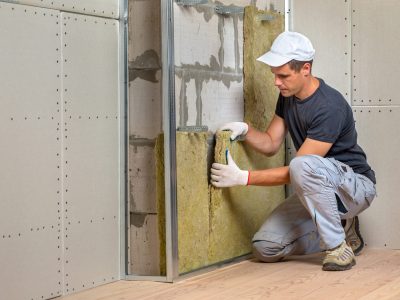 Worker insulating a room wall with mineral rock wool thermal insulation.